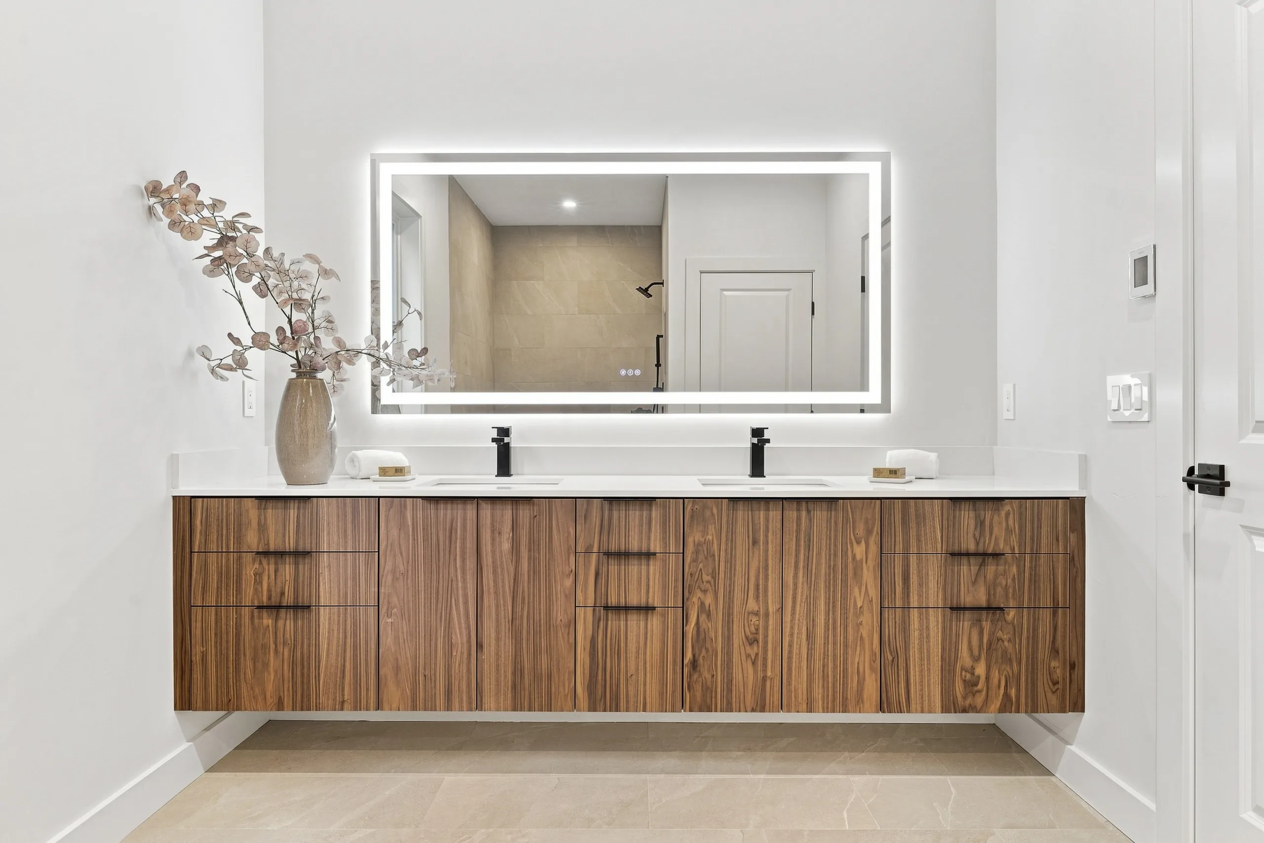 Primary bath with walnut double vanity and lit mirror